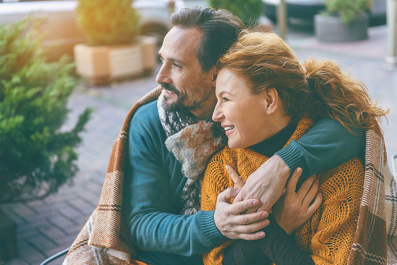 Happy loving couple is embracing and smiling. They are sitting outdoors covered by blanket