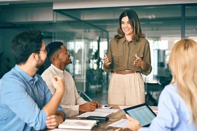 Happy middle aged business woman executive ceo leader discussing project management planning strategy working with diverse colleagues company team at office corporate board group meeting.