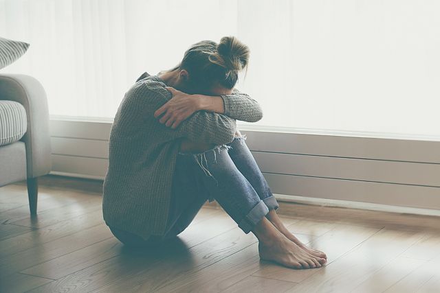 A lonely young woman feels depressed and stressed as she sits on the floor with her head in her hands.