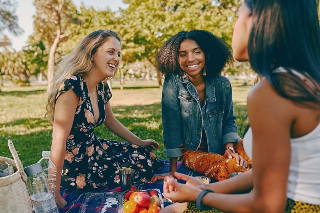 Smiling multiracial female friends having fun at picnic in the park - group of healthy friends having a picnic